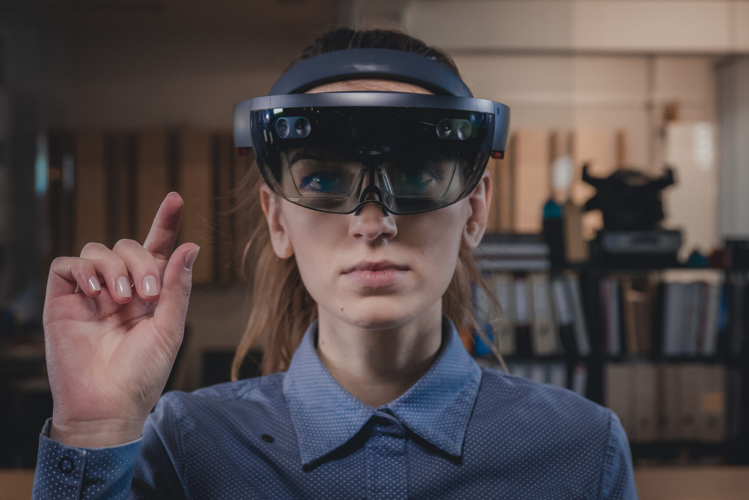 A woman wearing a blue shirt with a HoloLens 2 headset on interacting with AR.